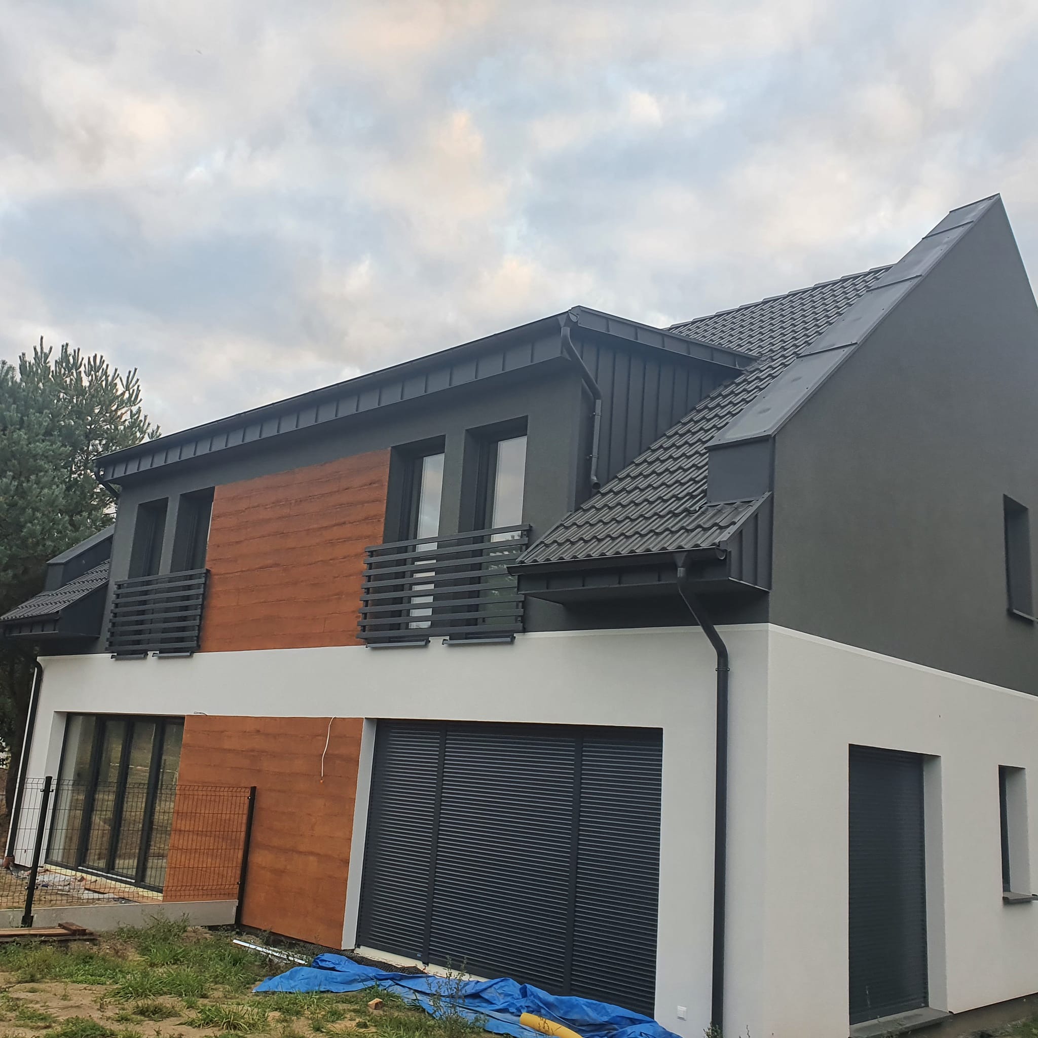 Nowoczesny dom z szarą dachówką karpiówką, grafitowymi rynnami i drewnianą elewacją na piętrze. Widoczne okna z grafitową stolarką. Ujęcie z dołu.