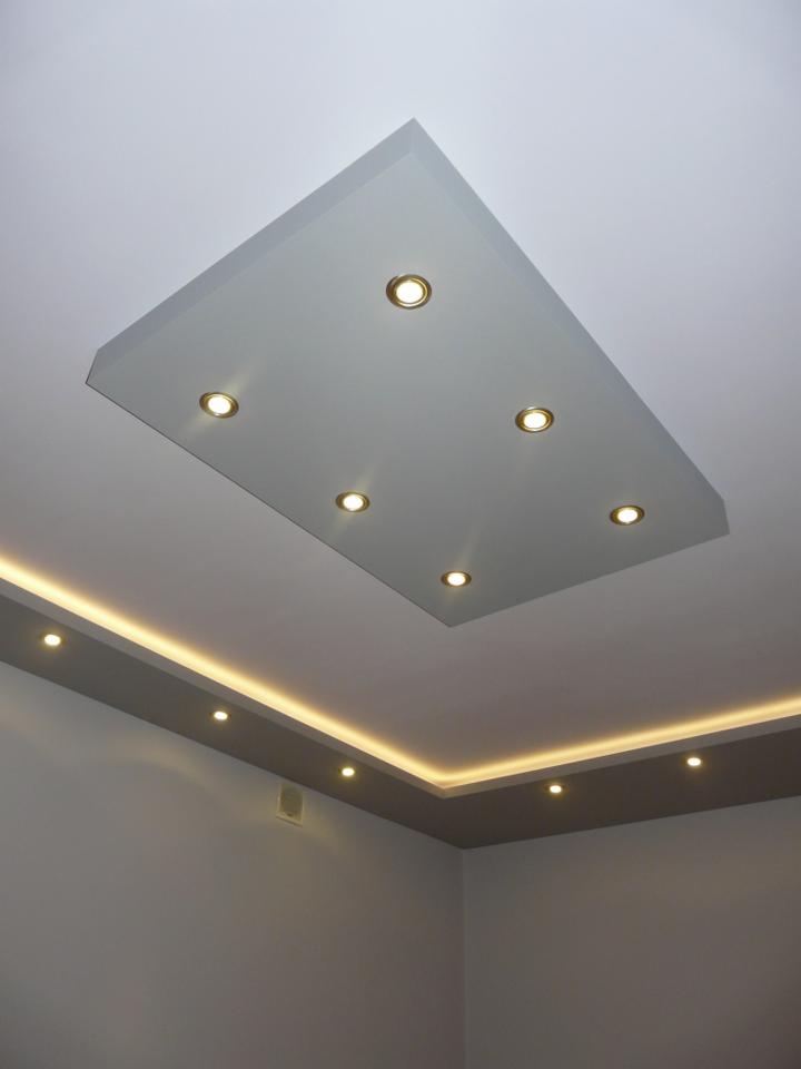 Podwieszany sufit z oświetleniem punktowym i listwą LED wzdłuż ściany, szare ściany. Widok z dołu, oświetlenie ciepłe.