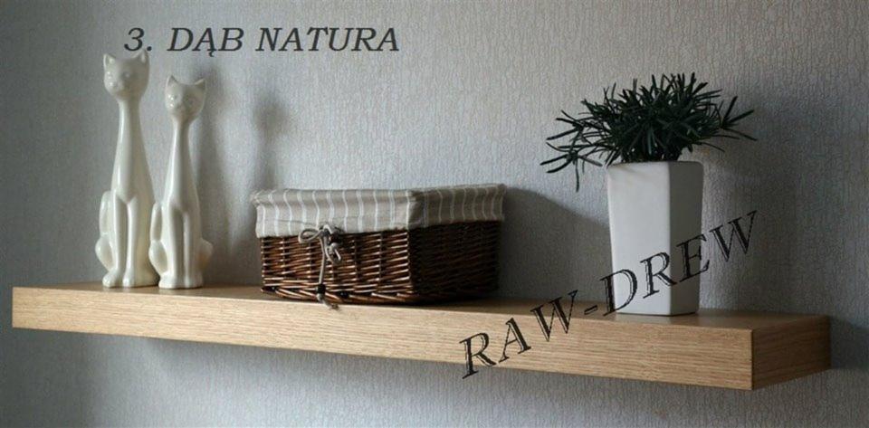 Półka dębowa 'Natura' z dekoracjami: dwie białe figurki kotów, wiklinowy koszyk i wazon z zieloną rośliną na tle jasnej ściany. Widoczny napis RAW-DREW.