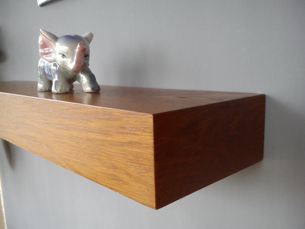 Drewniany parapet w odcieniach brązu, zamontowany na szarej ścianie, z figurką słonia na górze. Widoczna struktura drewna i minimalistyczny design.