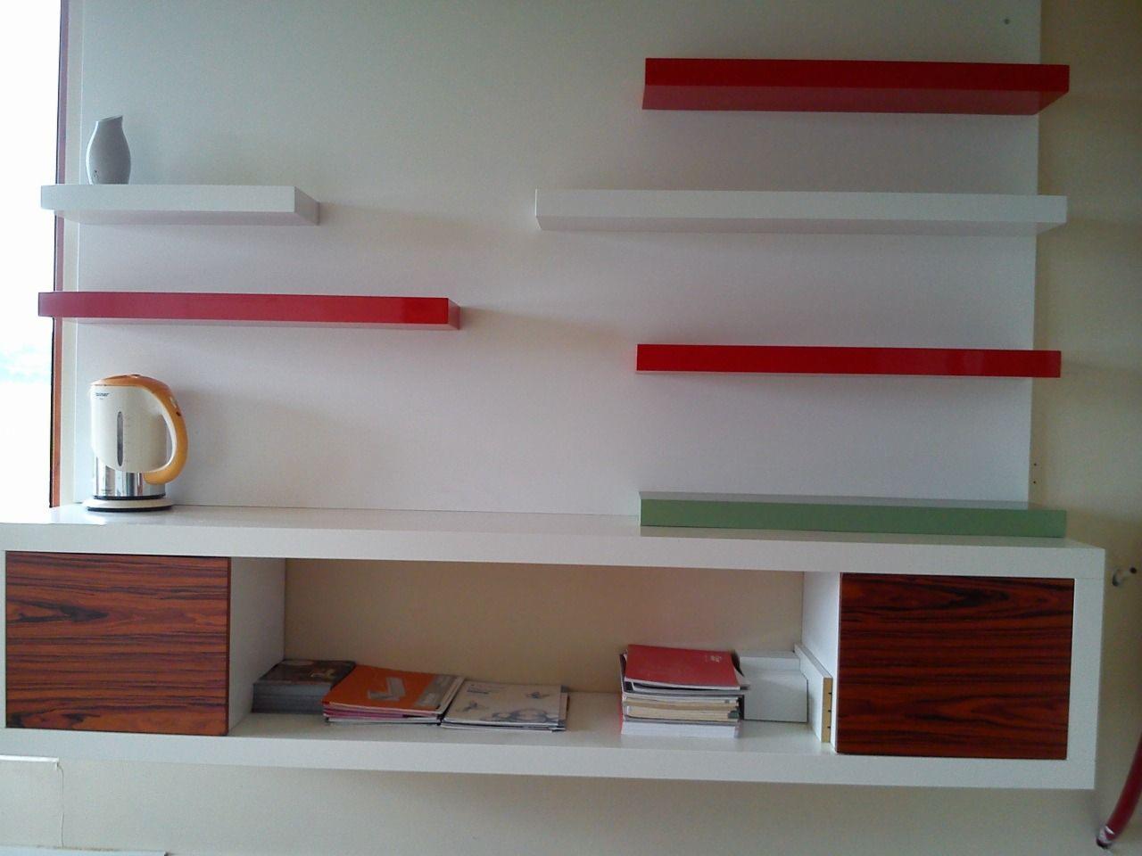 Białe półki wiszące z czerwonymi akcentami i szafkami z fornirem w Lelowie. Nowoczesny design, minimalistyczny styl. Na półkach czajnik i dekoracje.