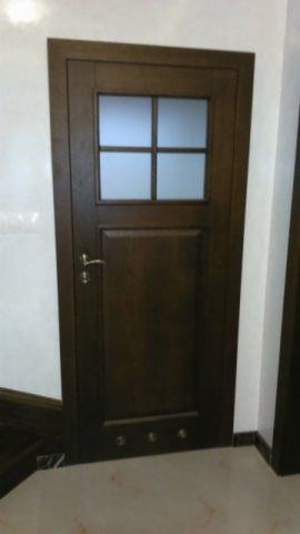 Ciemnobrązowe drzwi wewnętrzne z czterema szybkami z matowego szkła, zamontowane w jasnym pomieszczeniu. Widoczne detale wykończenia i metalowa klamka.