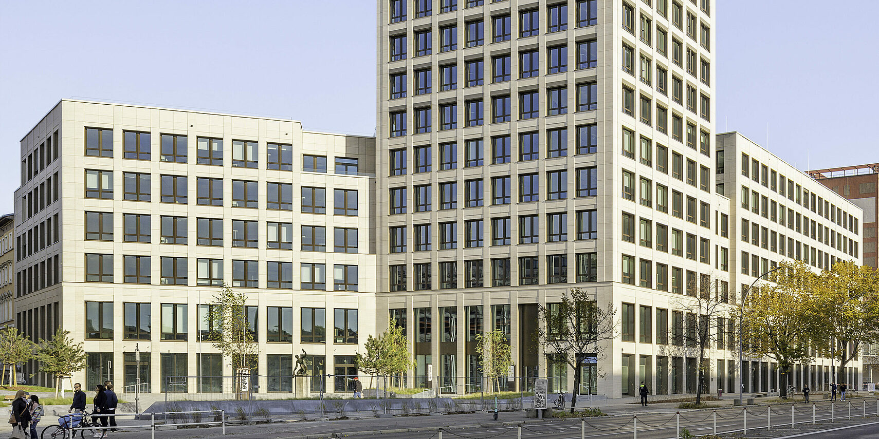 Nowoczesny budynek biurowy z jasną fasadą, licznymi oknami i drzewami wzdłuż ulicy, widok z poziomu ulicy.