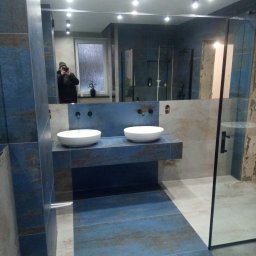 KMR-BUD Mariusz Moskal - Nowoczesna łazienka z dwoma białymi umywalkami nablatowymi na niebieskim blacie imitującym kamień, duże lustro z odbiciem osoby robiącej zdjęcie telefonem, kabina prysznicowa ze szklaną ścianką...