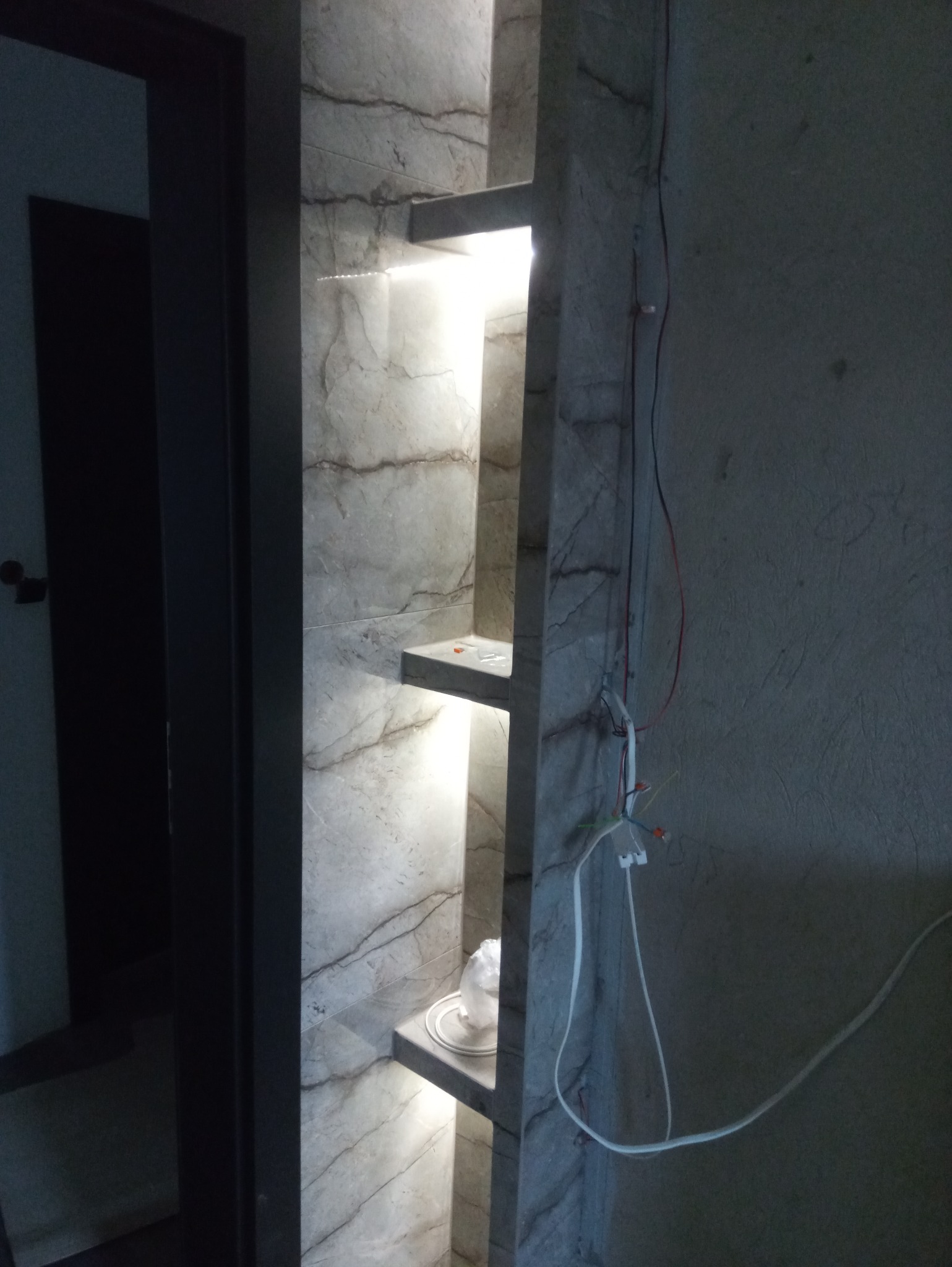 Wykończenie łazienki w Koninie: półki z podświetleniem LED, imitacja marmuru na ścianach, widoczne przewody elektryczne w trakcie montażu.