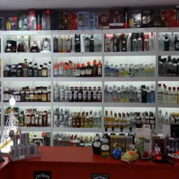 Półki sklepowe wypełnione różnorodnymi butelkami alkoholi, widoczne również elementy dekoracyjne na ladzie, takie jak ozdobne butelki i zabawkowy samochód.