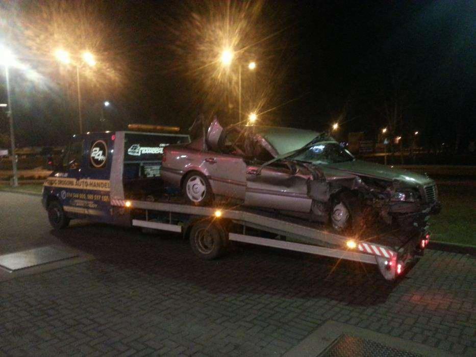 Laweta z uszkodzonym samochodem Mercedes na platformie, nocne oświetlenie uliczne. Widoczny numer telefonu na lawecie.