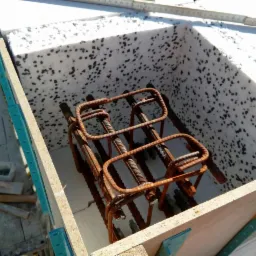 Zbrojenie w szalunku z izolacją styropianową, przygotowane do zalania betonem, widoczne elementy drewniane szalunku i narzędzia murarskie w tle.