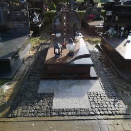 Sw-Bud sp. z.o. o - Granitowy nagrobek z lampionami i zniczami otoczony ciemną kostką brukową i jasnymi płytami na cmentarzu, po deszczu.