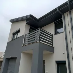 Nowoczesny dom dwukondygnacyjny z szarą, poziomą balustradą balkonową, szarymi oknami z roletami i szarą elewacją w dolnej części.