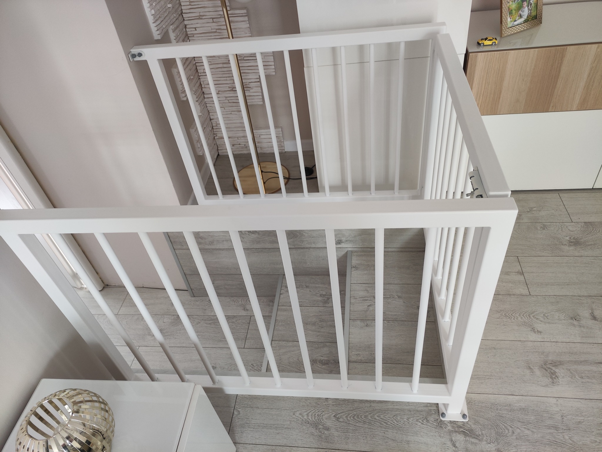 Biała, metalowa barierka ochronna zamontowana na schodach, widok z góry, jasne wnętrze z panelami podłogowymi.