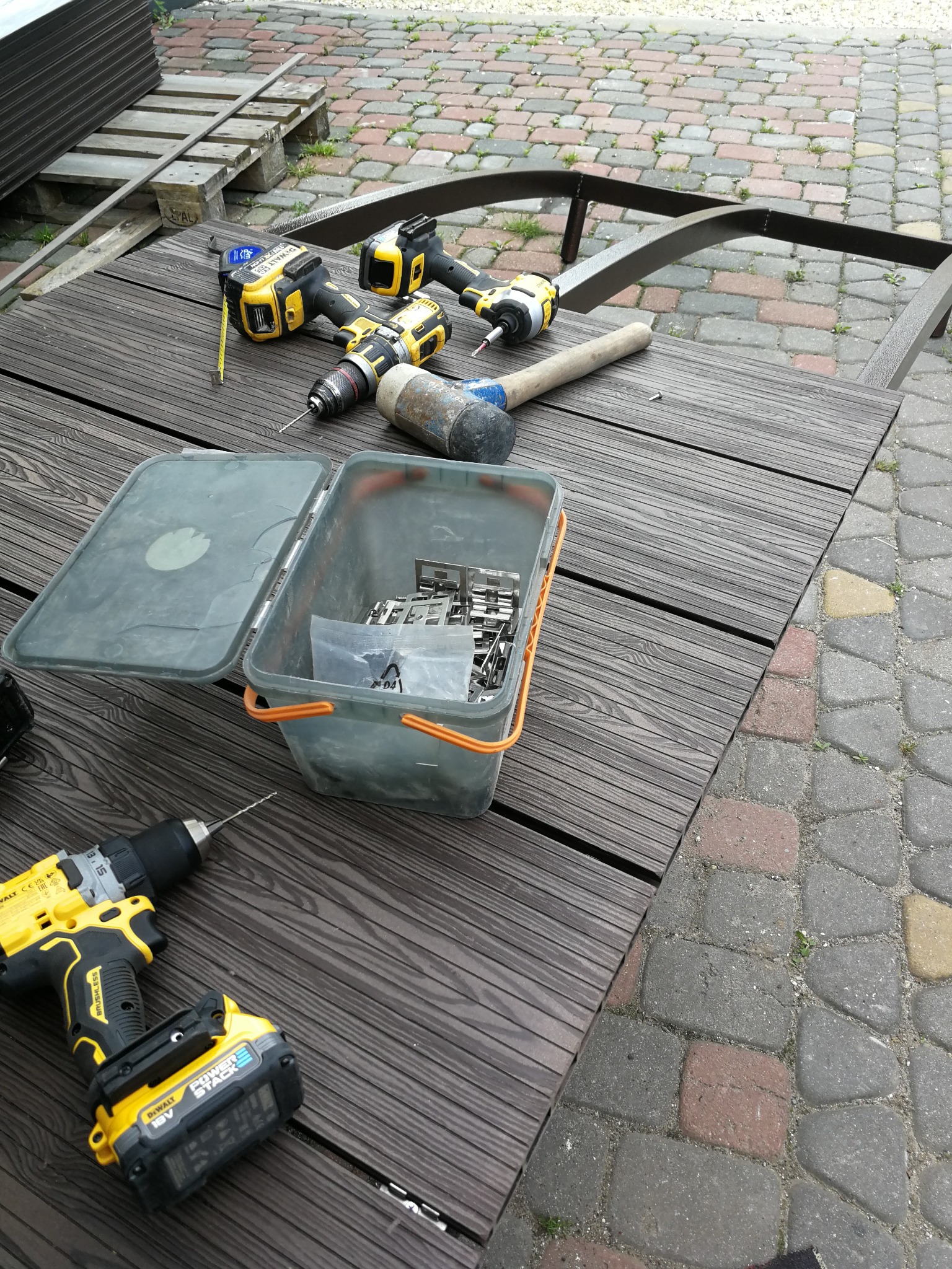 Narzędzia (wiertarki, młotek gumowy, miara) i elementy montażowe na desce tarasowej kompozytowej w trakcie budowy tarasu.