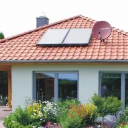 Dom jednorodzinny z szarymi oknami, czerwonym dachem z panelami solarnymi i anteną satelitarną. Ogród z kwiatami i zadaszone wejście.