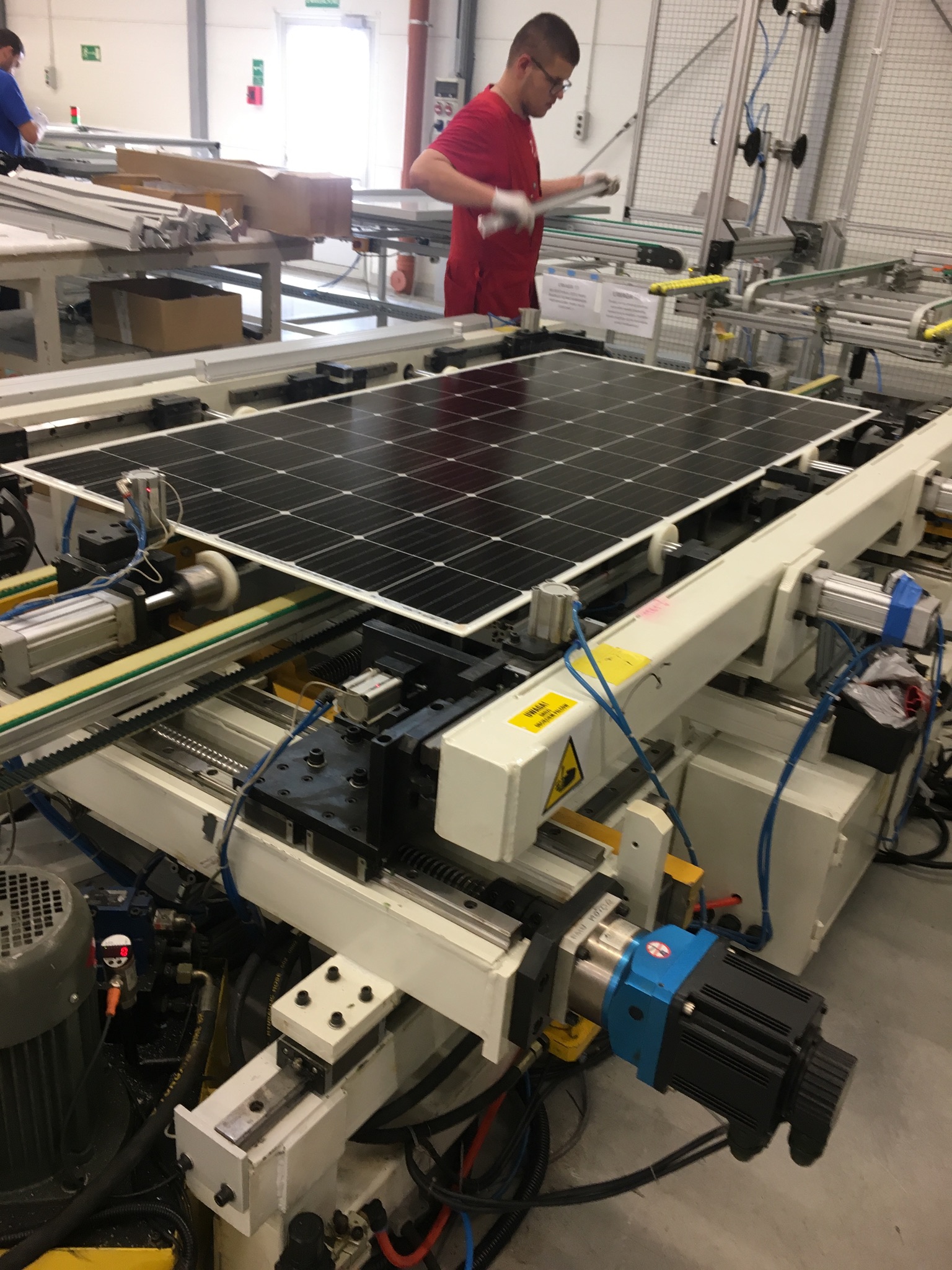 Panel słoneczny na linii produkcyjnej w fabryce, pracownik w czerwonej koszulce kontroluje jakość.