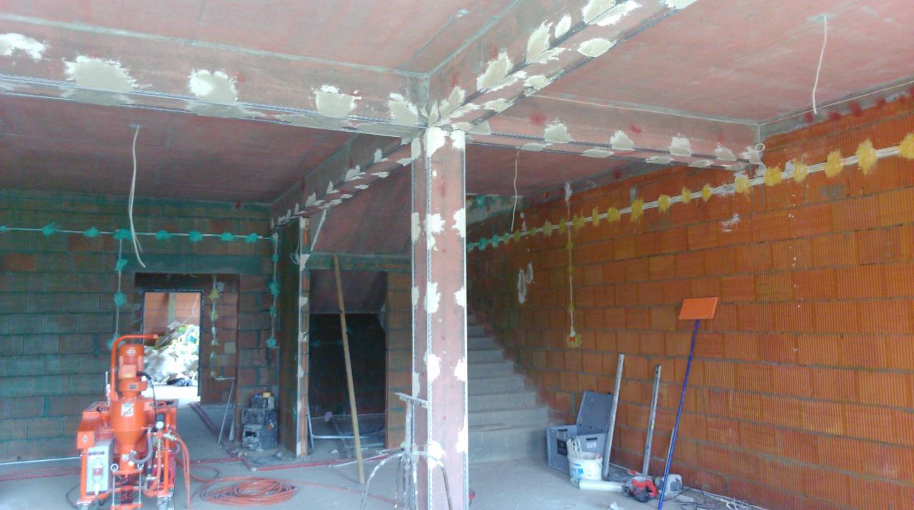 Przygotowanie do nałożenia gładzi w Wielkiej Wsi: widoczne ceglane ściany, metalowe wzmocnienia, instalacje elektryczne i sprzęt do tynkowania.