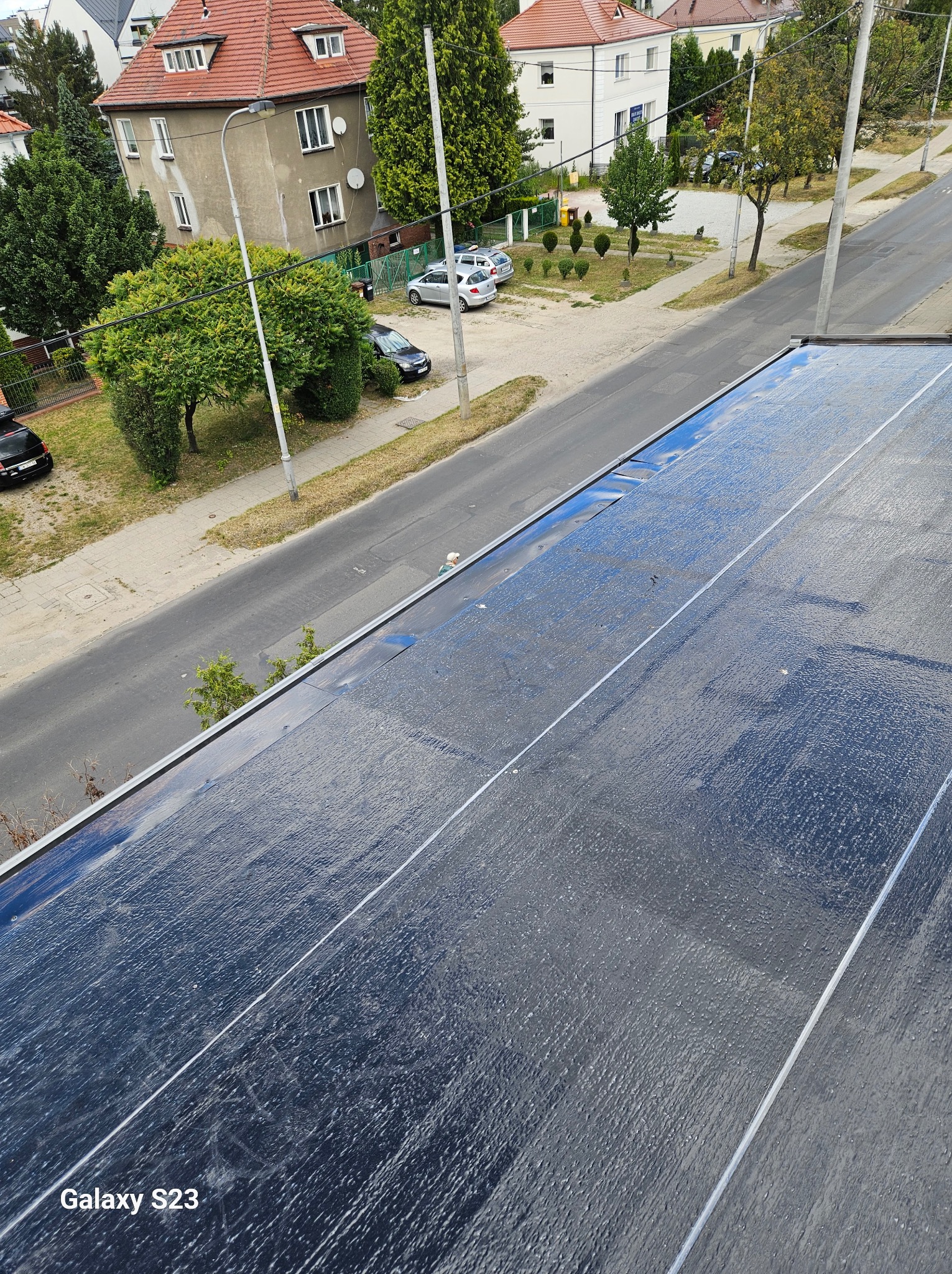 Nowe pokrycie dachu z papy termozgrzewalnej na tle ulicy i zabudowań miejskich. Widok z góry, ukazujący strukturę i detale wykonania.