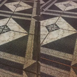 Częściowo wyczyszczona podłoga z płytek w geometryczne wzory, ukazująca różnicę w wyglądzie przed i po sprzątaniu fug. Widoczne zabrudzenia na jednej połowie.