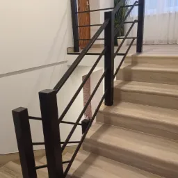 Nowoczesna klatka schodowa z drewnianymi stopniami i czarną, minimalistyczną balustradą z metalowymi prętami, widok z dołu schodów.