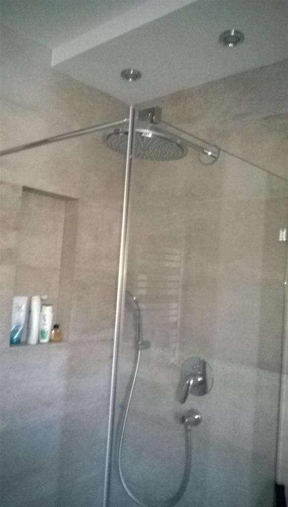 Kabina prysznicowa typu walk-in z deszczownicą i szarymi płytkami w łazience w Knurowie, z widoczną wnęką z kosmetykami.