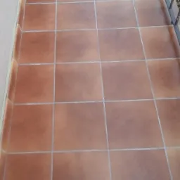 Ułożone, brązowe płytki na balkonie, widoczne białe fugi i fragmenty balustrady. Neutralne oświetlenie podkreśla regularny wzór.