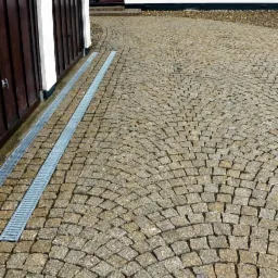 Ułożona kostka brukowa w kształcie wachlarza z odwodnieniem liniowym przy bramie garażowej.