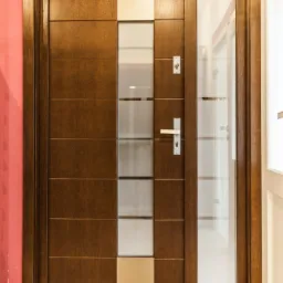 Brązowe skrzydło z przeszkleniami w pionowym układzie, srebrna klamka, widoczne fragmenty ściany w kolorze łososiowym i beżowe płytki podłogowe.