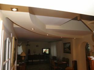 Nowoczesny, wielopoziomowy sufit podwieszany z oświetleniem punktowym w salonie. Wykończenie wnętrz w Toruniu. Jasne kolory ścian i sufitu.