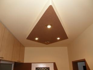 Brązowy, trójkątny sufit podwieszany z trzema punktowymi lampami w jasnym pomieszczeniu. Kontrastujące kolory i geometryczny kształt dodają wnętrzu nowoczesnego charakteru.