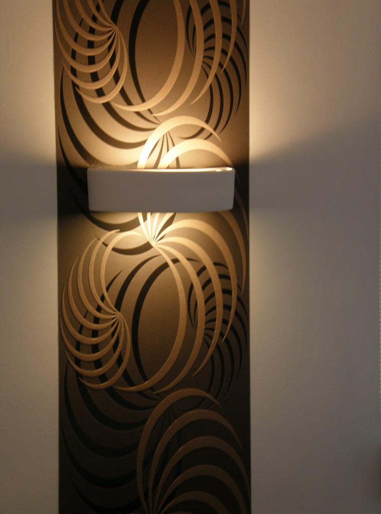 Oświetlona ściana z tapetą w geometryczne wzory, podkreślona przez nowoczesny kinkiet. Ciepłe światło akcentuje dekoracyjny charakter tapety.