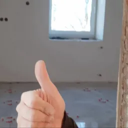 Mężczyzna daje kciuk w g&oacute;rę na tle remontowanej łazienki z nową podłogą i przygotowanymi punktami elektrycznymi na ścianie.