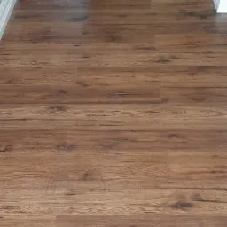 Ułożone brązowe panele podłogowe z widoczną strukturą drewna, w tle białe listwy przypodłogowe i fragment drzwi.