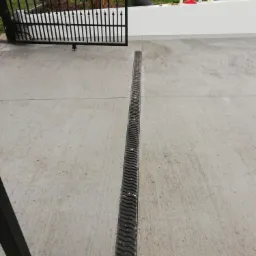 Wykończona betonowa nawierzchnia z odpływem liniowym, widok z perspektywy bramy wjazdowej.