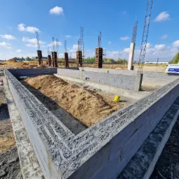Fundamenty domu jednorodzinnego z betonu komórkowego, zbrojenia pionowe, szalunki i hałda piasku wewnątrz, błękitne niebo w tle. Etap budowy w słoneczny dzień.