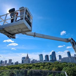klimatyzacjewarszawa.pl - Podnośnik koszowy z pracownikiem na tle panoramy Warszawy i błękitnego nieba z chmurami, widok z góry.