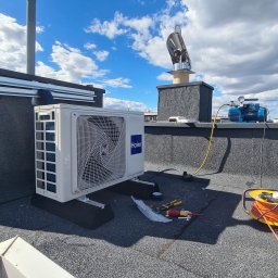 klimatyzacjewarszawa.pl - Biała jednostka zewnętrzna klimatyzacji Haier zamontowana na płaskim dachu, obok butla z gazem, pompa próżniowa i zwinięty przedłużacz. Widoczne narzędzia i elementy instalacji.