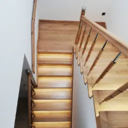 Widok z góry na drewniane schody z podświetleniem LED w Zamościu, z metalowo-drewnianą balustradą i białymi ścianami.