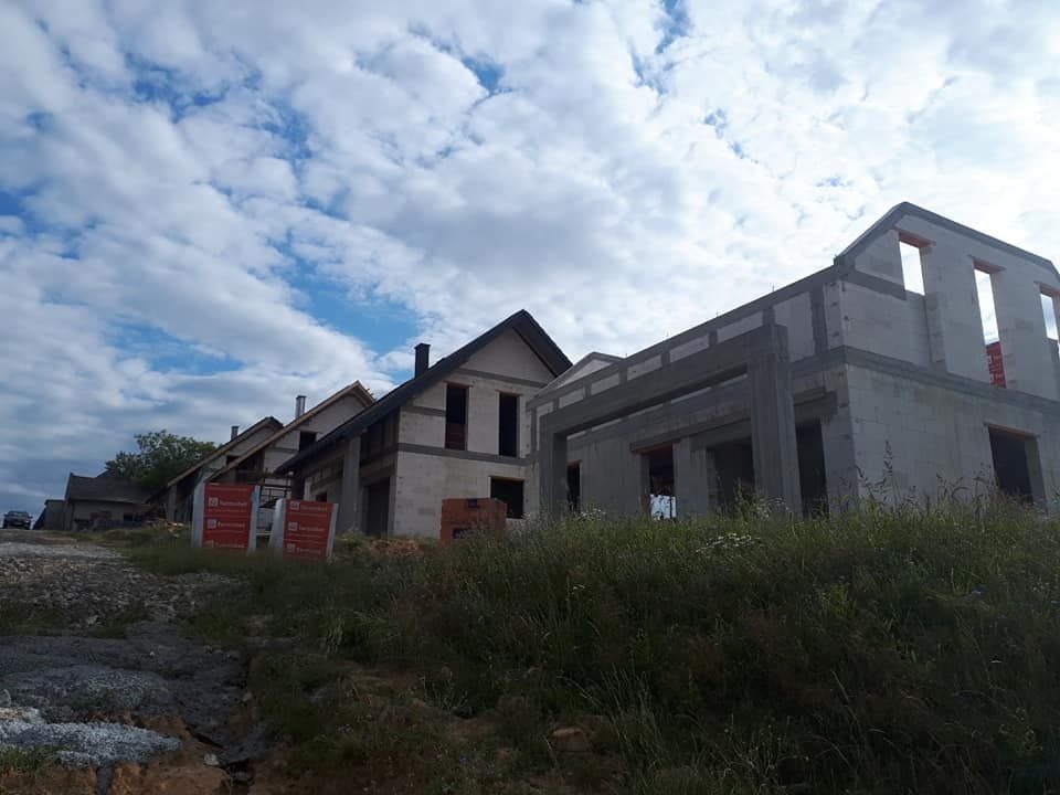 Rząd domów w trakcie budowy z betonu komórkowego, z widocznymi otworami okiennymi i zarysami dachów, na tle pochmurnego nieba.