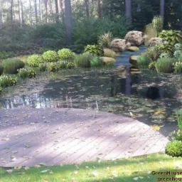 Projekt ogrodu z drewnianym tarasem nad stawem, otoczonym roślinnością i kamieniami. W tle widoczny las. Wizualizacja z elementami fotorealizmu.