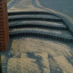 Ułożona kostka brukowa na podjeździe z zaokrąglonymi schodami wykonanymi z obrzeży betonowych, widok z góry na świeżo ułożoną nawierzchnię z widocznym piaskiem wypełniającym szczeliny.