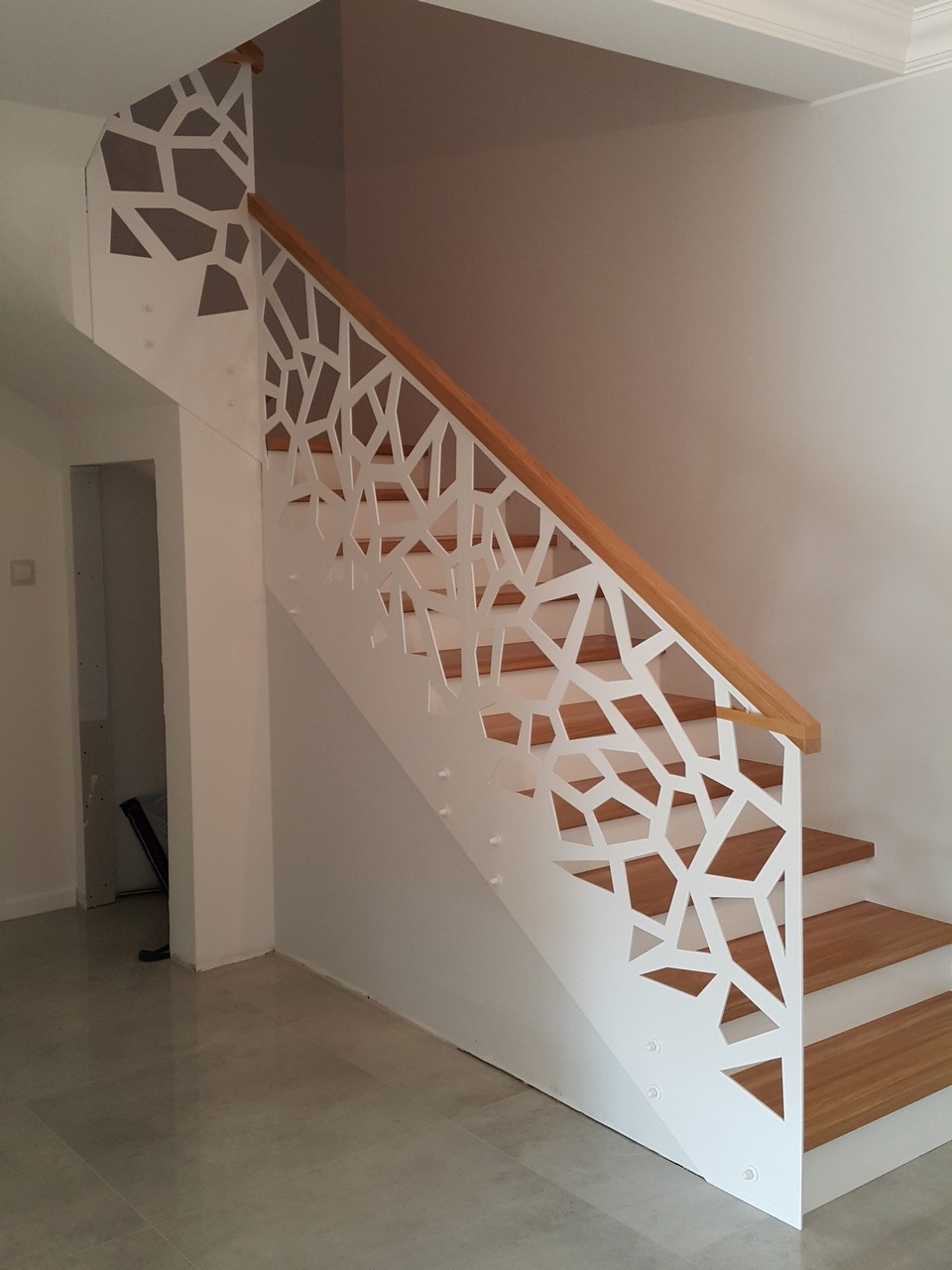 Nowoczesne schody z drewnianymi stopniami i białą, ażurową balustradą z geometrycznym wzorem, drewniana poręcz, jasne wnętrze.