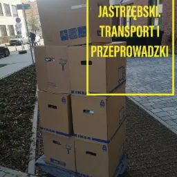 Stos kartonowych pudeł IKEA, oznaczonych jako 30 kg, ustawionych na wózku transportowym, przed budynkiem mieszkalnym.