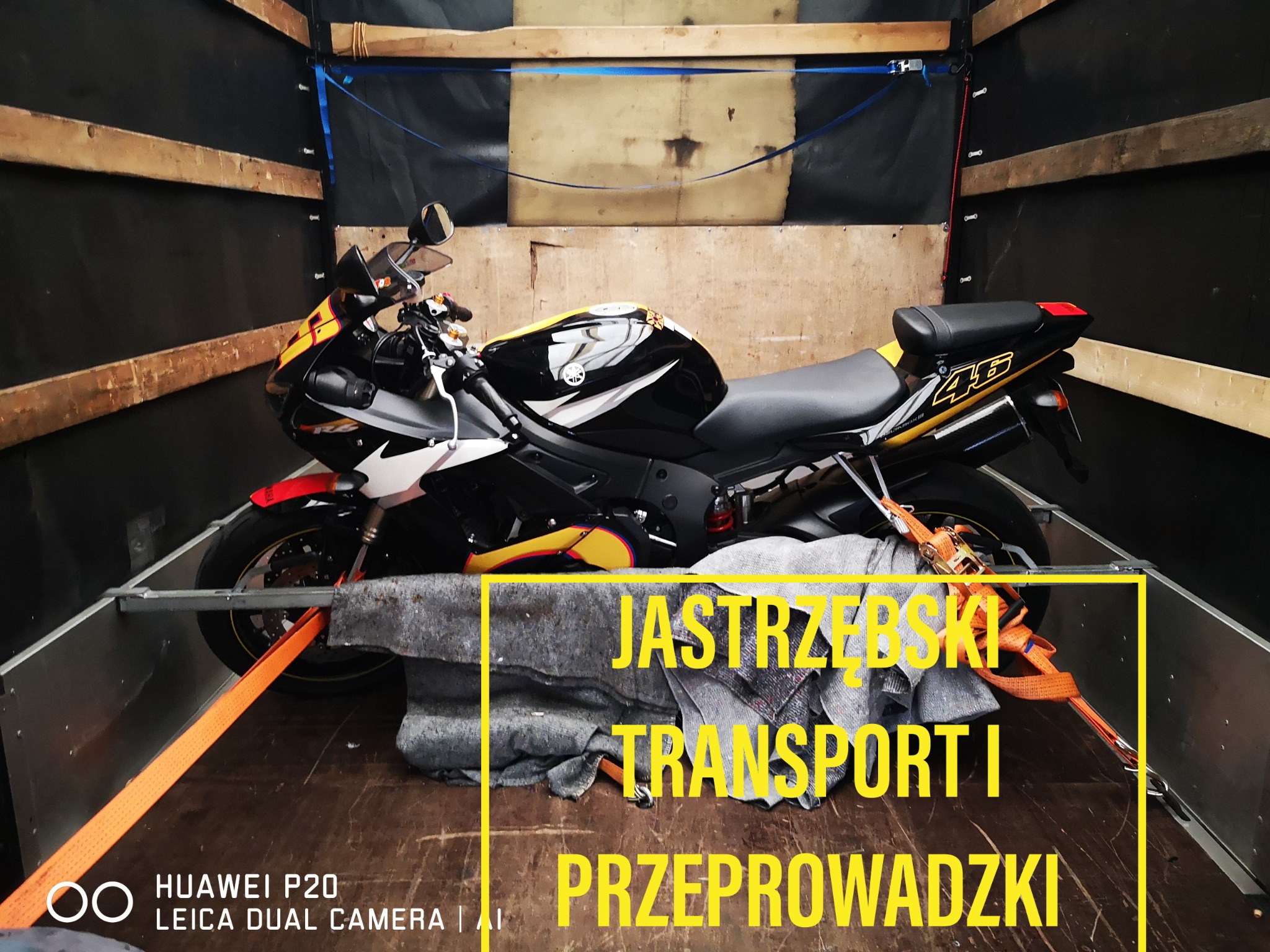 Czarno-żółty motocykl sportowy zabezpieczony pasami transportowymi wewnątrz drewnianej furgonetki, przygotowany do transportu.
