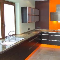 Nowoczesna kuchnia z ciemnymi szafkami, granitowym blatem i pomarańczowym panelem ściennym za srebrnym okapem. Widoczny zlew przy oknie z ceglaną ścianą.
