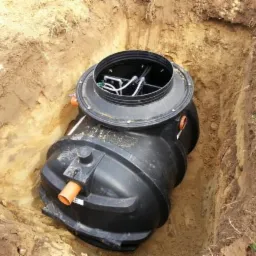 Czarna przydomowa oczyszczalnia ścieków BioPura umieszczona w wykopie ziemnym z widoczną pokrywą i elementami instalacji wewnętrznej.