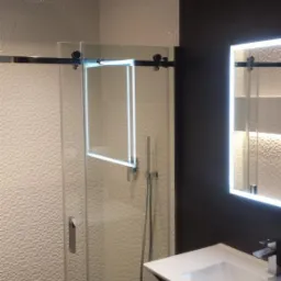 Nowoczesna łazienka z kabiną prysznicową przesuwną, wykończona jasnymi, teksturowanymi płytkami i czarnymi elementami, oświetlona punktowo i z lustrem z podświetleniem LED.