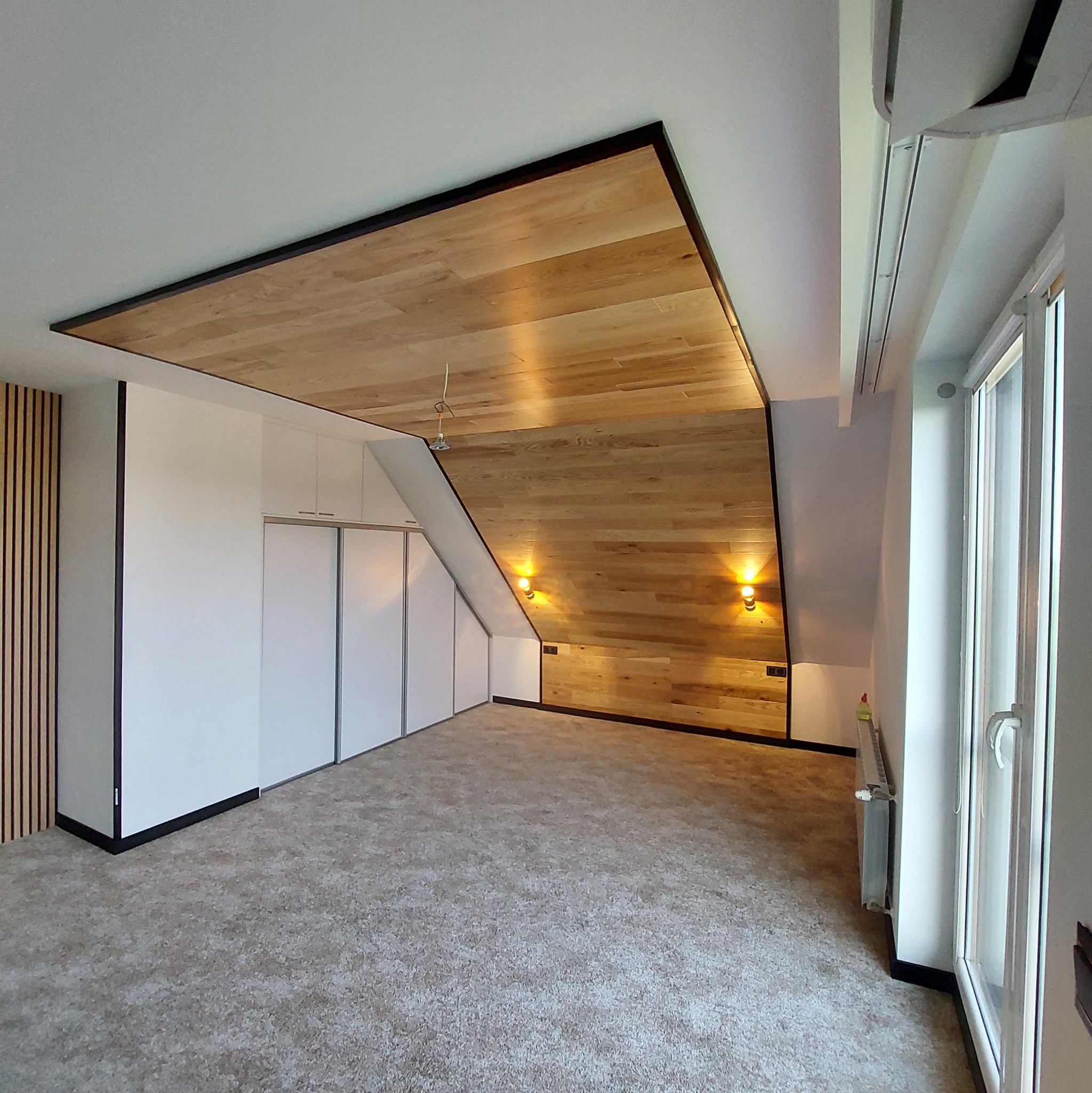 Wykończone poddasze z drewnianą boazerią na suficie i ścianie, oświetleniem punktowym, zabudową szaf i grzejnikiem pod oknem.