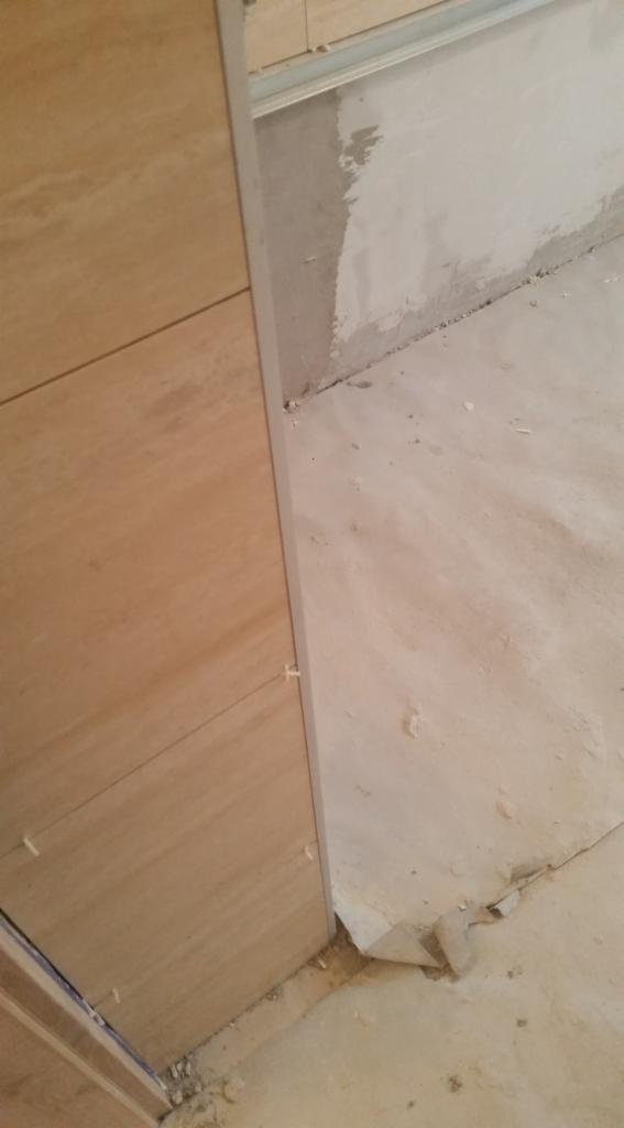 Beżowe płytki ścienne z krzyżykami dystansowymi, widoczne surowe ściany i podłoga w trakcie prac wykończeniowych.