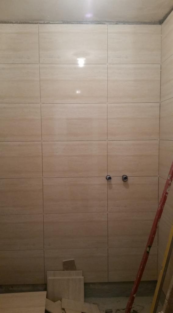 Beżowe płytki imitujące drewno, ułożone na ścianie w łazience. Widoczne dwa otwory na armaturę, resztki płytek na podłodze i drabina oparta o ścianę.