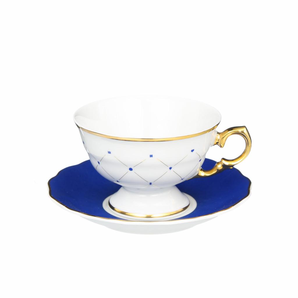 Biała filiżanka z niebieskim wzorem i złotym obramowaniem na granatowym spodku z falowaną krawędzią, na białym tle.