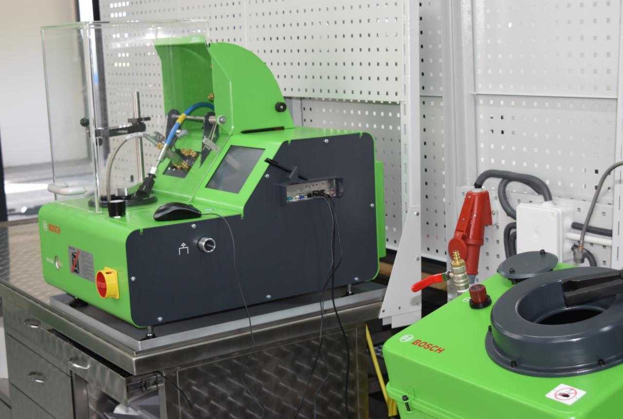 Profesjonalne urządzenie diagnostyczne Bosch do testowania wtryskiwaczy paliwa, umieszczone w warsztacie z perforowanymi ścianami.